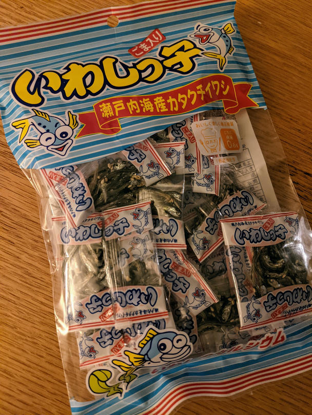 The big, unopened bag of iwashikko on my oaken coffee table. Inside are lots of little bags with tiny sardines curled in improbably positions with a few sesame seeds on them. The fish on the front is winking at you, like he was somehow despised the 200 little fishies in this big bag, or perhaps he was even somehow responsible?
