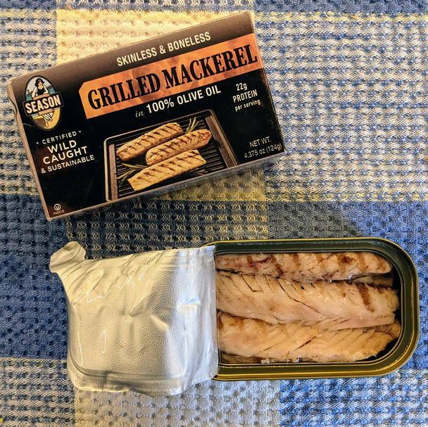 the black box next to the open tin on a checkered towel. peel-back foil lid! fillets are dense, glistening under pale olive oil. grill marks are present, but not overwhelming
