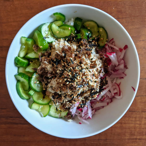 a white ceramic bowl on my teak veneer dining room table. a mound of mackerel-mayo topped with furikake sits on rice; green halfmoons of misozuke on the left, slivers of red-and-white radish on the right
