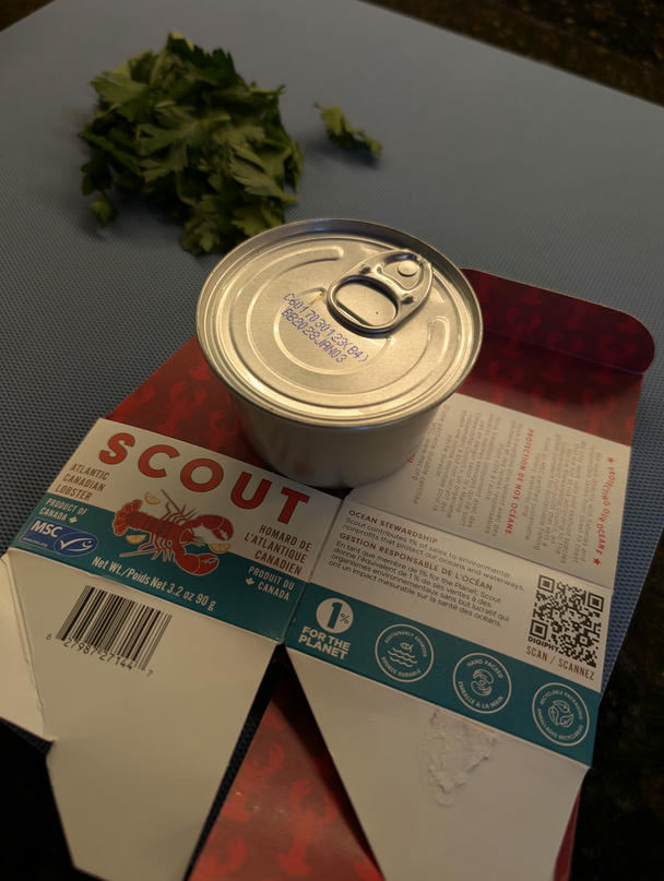 the unopened tin sits on the flattened box; behind, parsley awaits the knife.
